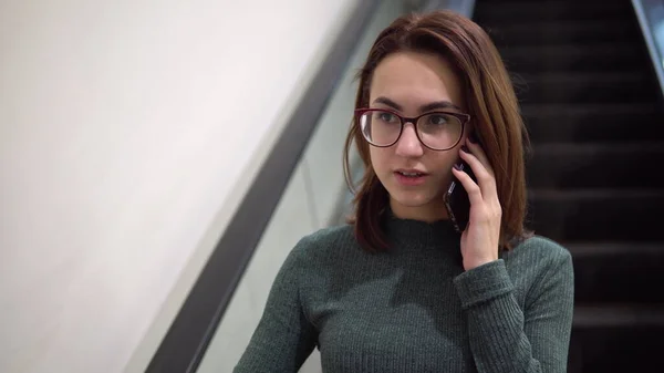 若い女性がエスカレーターに乗って電話で話す。大型ショッピングセンター — ストック写真