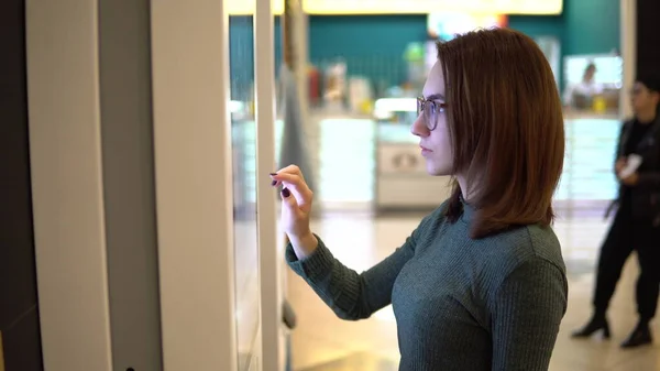 Genç bir kadın alışveriş merkezindeki dokunmatik terminalden yemek sipariş ediyor. Modern teknoloji. Yemek katında sırada beklemeden.