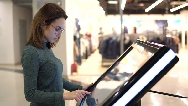 Genç bir kadın alışveriş merkezindeki elektronik dokunmatik bir masada navigasyon haritasını izliyor..