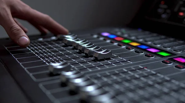 Adam profesyonel bir elektronik ses mikseri üzerinde çalışıyor. Ses kanallarını ayarlamak için bir kontrol paneli.