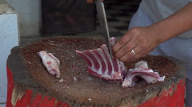 Bir adam satırla doğruyor. Taze et ve koç eti. İnsan kızarmak için kemik keser.