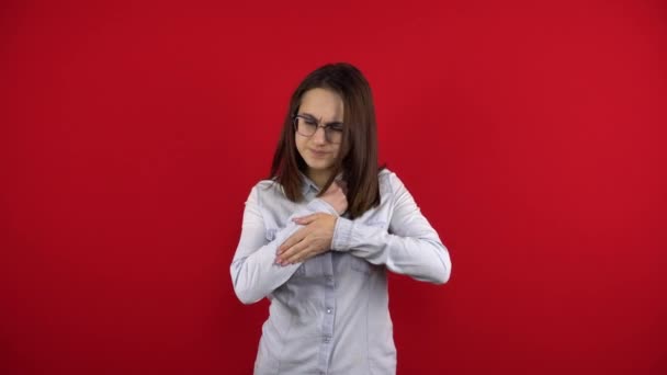 Mladá žena má na paži obvaz a dotýká se bolavé paže. Natáčení na červeném pozadí. — Stock video