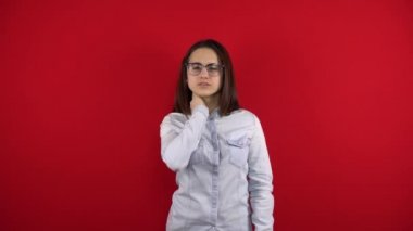 Gözlüklü genç bir kadının boynunda bir ağrı var, eliyle boynunu tutuyor. Kırmızı arkaplanda çekim.