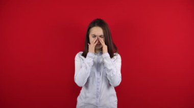 Genç kadının burnu ağrıyor, eliyle dokunuyor. Kırmızı arkaplanda çekim.