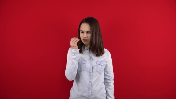 A jovem tem um nariz dolorido, toca-lhe com a mão. Tiro em um fundo vermelho. — Vídeo de Stock