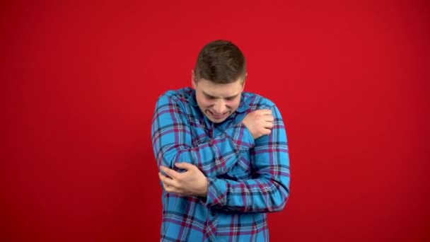 A young man has a sore elbow and holds it in his hand. Shooting on a red background. — Stock Video