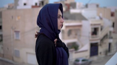 Arap türbanlı genç kadın. Çatıda bir kadın yürüyor. Evin çatısında, Arap evlerinin arka planına karşı..