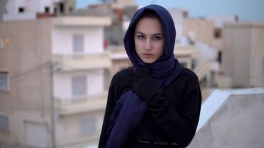 Arap türbanlı genç kadın. Çatıda bir kadın yürüyor. Evin çatısında, Arap evlerinin arka planına karşı..