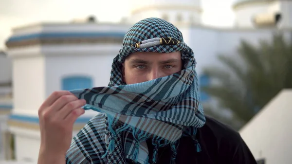 Молодой человек в арабском платке. Человек закрывает лицо. На фоне арабского дома. — стоковое фото