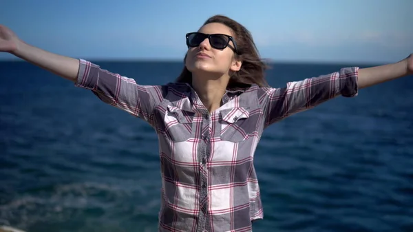 La joven levantó las manos contra el telón de fondo del mar. Chica con gafas de sol en tiempo soleado. Chica consigue placer. — Foto de Stock