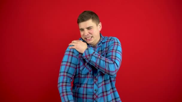 A young man has a sore shoulder and he touches it with his hand. Shooting on a red background. — Stock Video