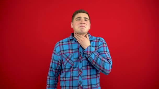 A young man has a sore throat and she touches him with his hand. Shooting on a red background. — Stock Video