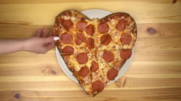 バレンタインデーのハート型のピザ。若い女性はピザのトップビューのスライスを取ります. — ストック動画