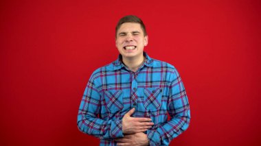 Genç bir adamın midesi ağrır ve onu elinde tutar. Kırmızı arkaplanda çekim.