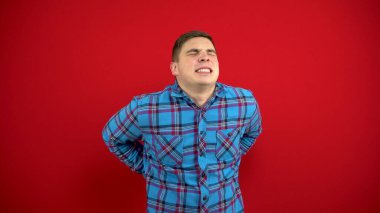 Genç bir adamın sırt ağrısı var ve onu elinde tutuyor. Kırmızı arkaplanda çekim.