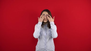 Genç kadınların gözleri acıyor. Elleriyle masaj yapıyor. Kırmızı arkaplanda çekim.