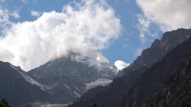Gökyüzünde bulutlu yüksek karlı dağların manzarası.