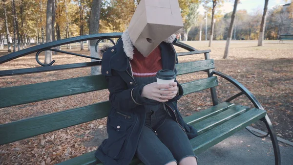 The girl with the package on his head sitting on a bench with a cup of coffee. Girl in a jacket