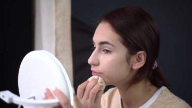 Genç bir kadın küçük bir aynaya bakar ve süngerle makyaj yapar. Cilt bakımı.