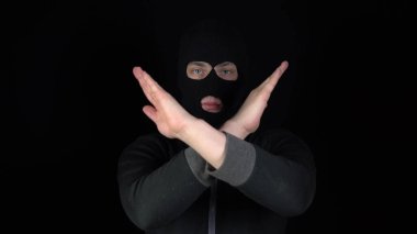 Kar maskesi takmış bir adam elleriyle negatif bir işaret gösterir. Eşkıya siyah bir arka planda kollarını kavuşturdu..