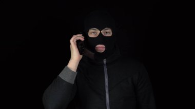 90 'lardan kalma telefonu olan kar maskeli bir adam. Haydut telefonda konuşuyor. Siyah bir arkaplanda.