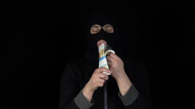 Kar maskeli bir adam elinde bir tomar rubleyle dikiliyor. Haydut parayı karıştırıyor ve seviniyor. Siyah bir arkaplanda.