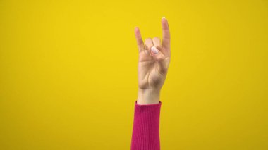 Kadın eli boynuzların işaretini gösterir. İzole edilmiş sarı arkaplanda stüdyo fotoğrafçılığı.