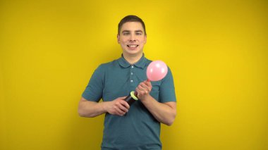 Genç bir adam sarı arka planda pompası olan pembe bir balonu şişiriyor. Yeşil polo giyen adam..