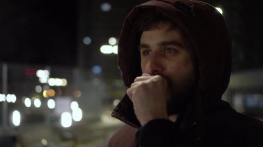 Genç bir adam dışarıda soğukta duruyor ve nefesiyle ellerini ısıtıyor..