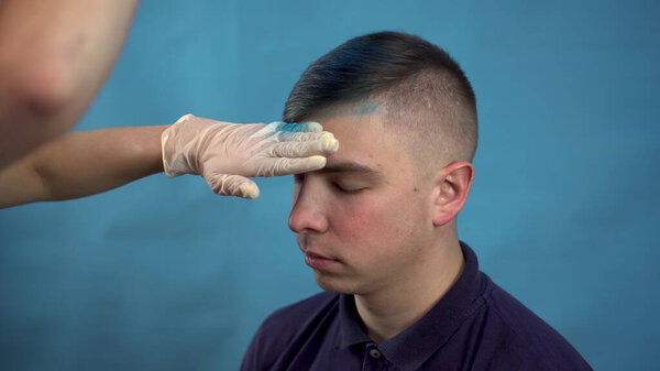 Молодой человек покрасил волосы в синий цвет. Альтернативный человек окрашивается временным спреем для волос. На синем фоне
