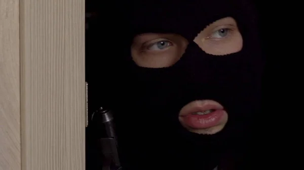 Burglar behind the door with a gun closeup. The masked thug slowly opened the door and went into the room.