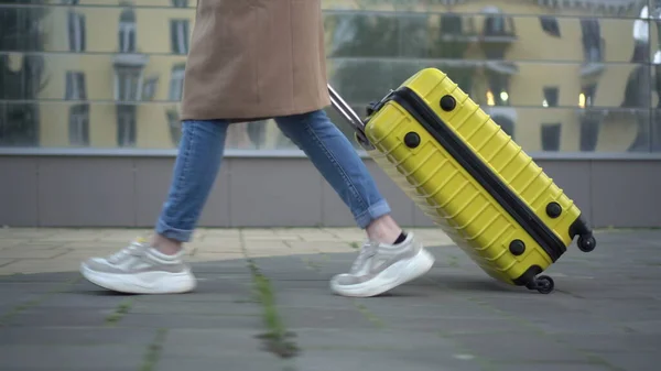 A young woman walks with a yellow suitcase closeup. Стоковая Картинка