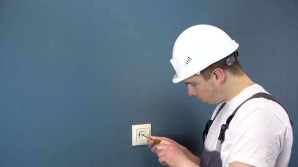 Un elettricista ripara una presa in casa. Un uomo in abiti speciali e un casco sta smontando uno sbocco. — Video Stock