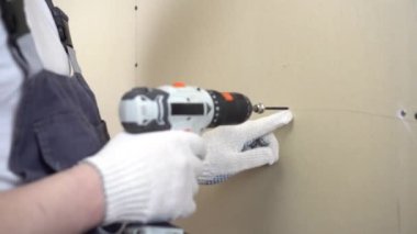 İnşaatçı, duvardaki tornavidayı kullanarak alçı taşı tahtasını kendi kendine tıkırdatıyor..