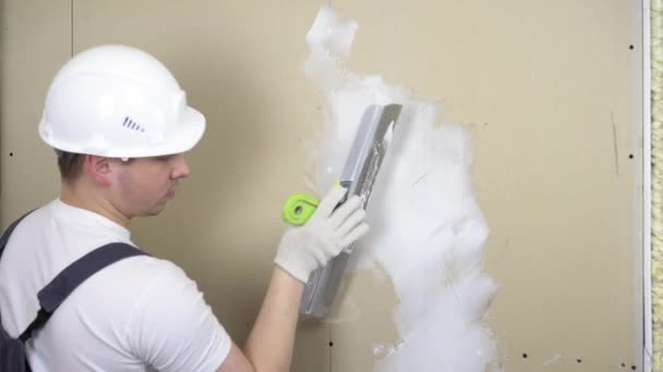 Der Bauarbeiter putzt die Wand im Raum. Ein Mann in Spezialkleidung und Helm repariert. — Stockvideo