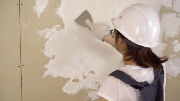 El constructor escayola la pared de la habitación. Una mujer con ropa especial y un casco hace reparaciones. — Vídeo de stock