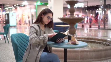 Bir kafede genç bir kadın fıskiyenin arka planına karşı bir kitap okuyor. Kafedeki dekorasyon..