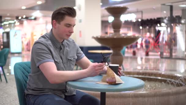 카페에 손에 전화기를 들고 분수의 배경에 기대어 있는 젊은이. 카페에 있는 장식. — 비디오