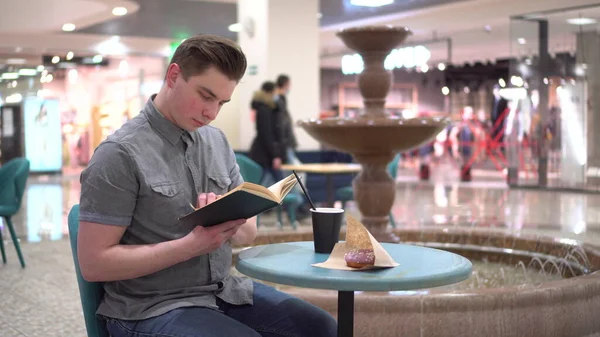 Молодий чоловік у кафе читає книгу на тлі фонтану. Декорування в кафе . — стокове фото