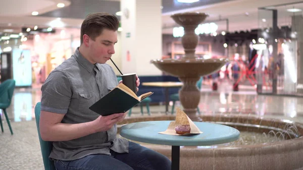 Молодий чоловік у кафе читає книгу на тлі фонтану. Декорування в кафе . — стокове фото