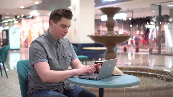 Jeune homme dans un café avec un ordinateur portable sur le fond d'une fontaine. Décoration dans le café. — Photo