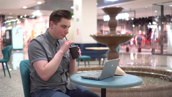 Молодий чоловік у кафе з ноутбуком на фоні фонтану. Декорування в кафе . — стокове фото