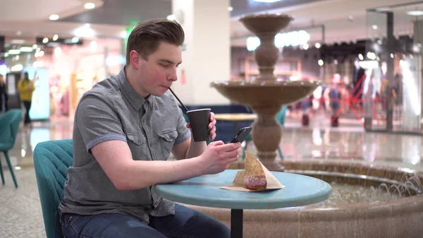 Молодий чоловік у кафе з телефоном у руках на тлі фонтану. Декорування в кафе . — стокове фото