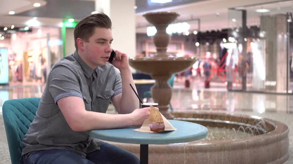 Молодой человек в кафе говорит по телефону на фоне фонтана. Украшение в кафе. — стоковое фото
