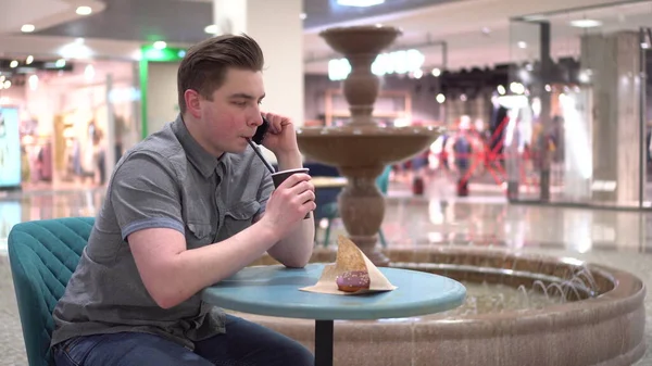 Молодой человек в кафе говорит по телефону на фоне фонтана. Украшение в кафе. — стоковое фото