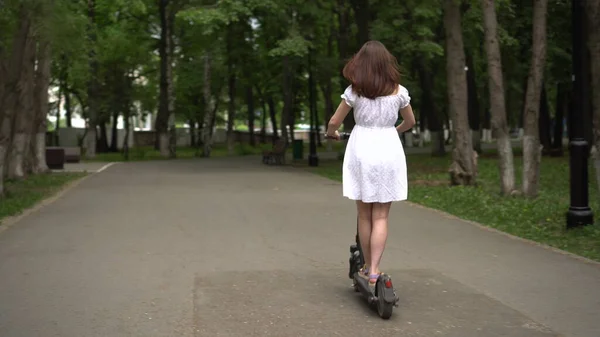 Jeune femme asiatique en robe blanche monte un scooter électrique de partage dans le parc. Fille dans des lunettes. — Photo