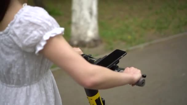 Una mujer joven en un vestido monta un electro scooter compartido. Volante de la vespa primer plano. — Vídeos de Stock