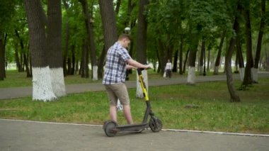 Gömlek ve şort giyen genç bir Avrupalı parkta elektrikli scooter 'ı paylaşıyor..