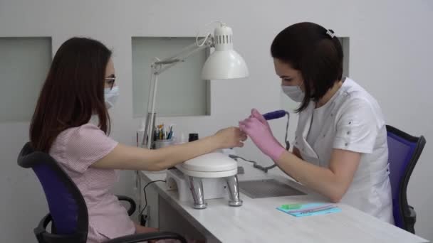 Ung kvinde med briller i en manicure salon. En manicurist bruger en boremaskine til at fjerne negle. – Stock-video