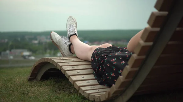一个穿着连衣裙和运动鞋的小女孩躺在草地上的躺椅上。女孩的腿靠得很近. — 图库照片
